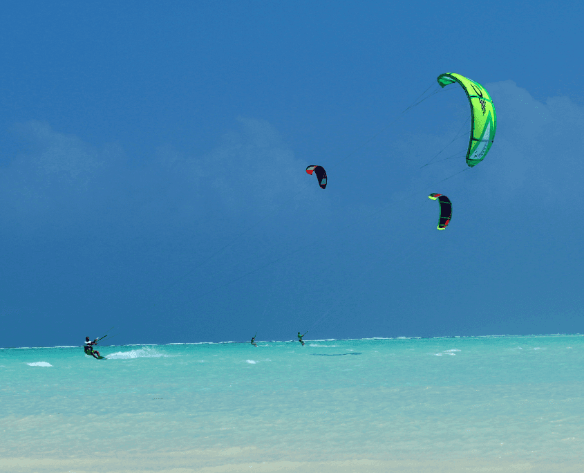 Kitesurfers op het turquoise water voor de kust van Paje